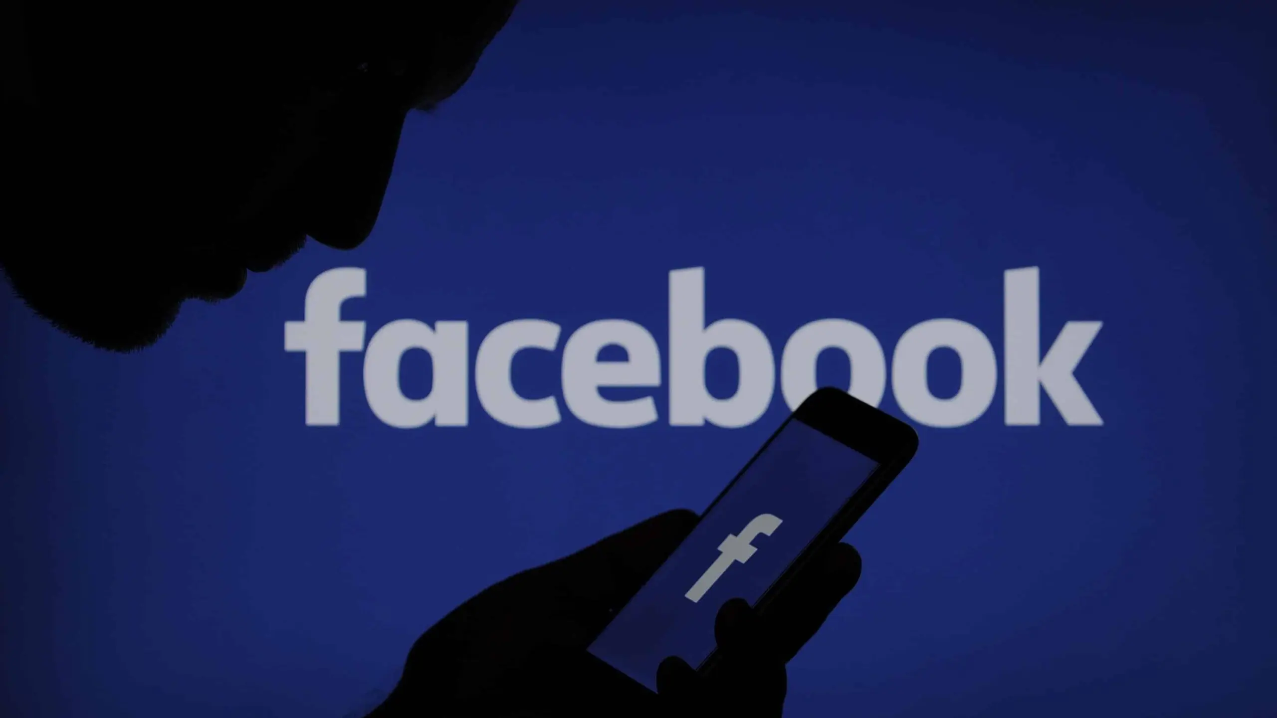 Foto ilustrativa mostra silhueta de pessoa com smartphone na mão, à frente de logo do Facebook, aplicativo da Meta
