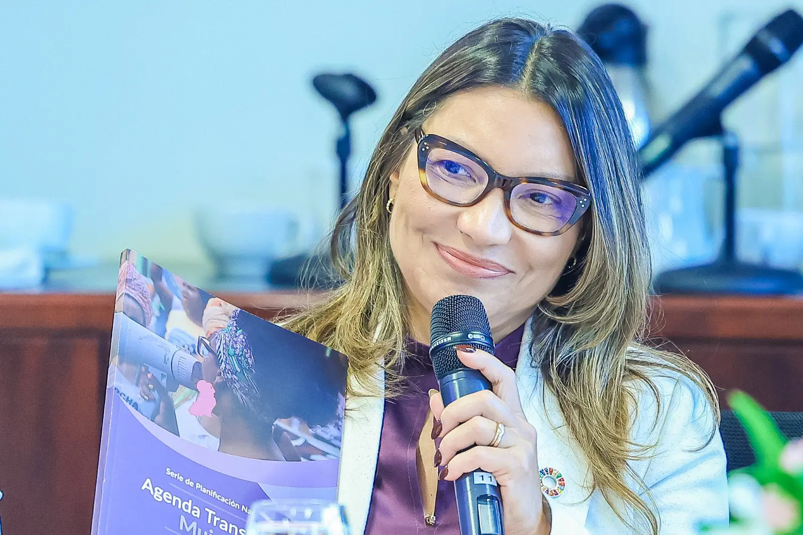 A primeira-dama, Janja, aparece sorrindo, com óculos e microfone nas mãos