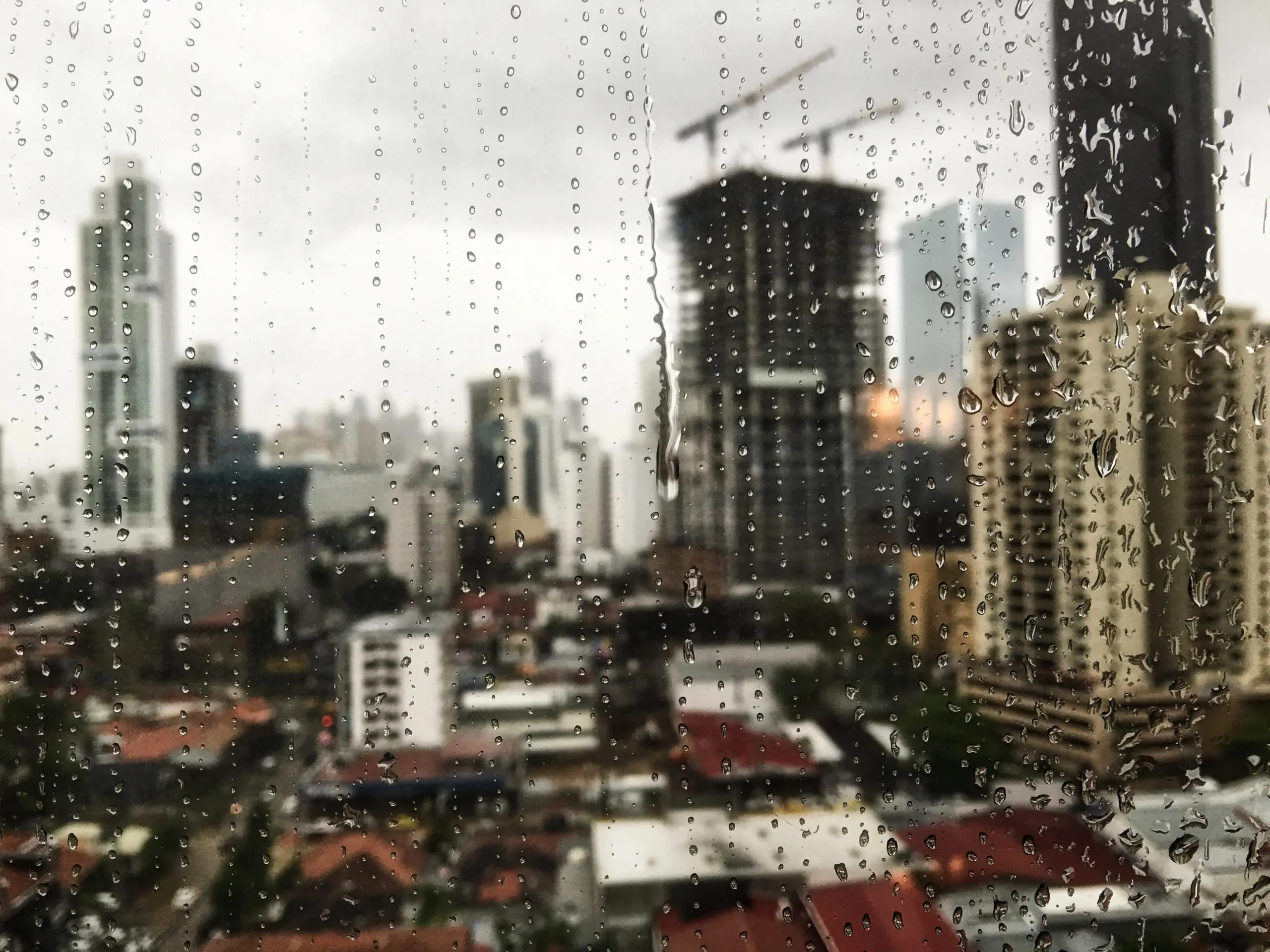 Janela que mostra uma cidade com prédios, e o vidro apresente gotículas de água, mostrando que choveu