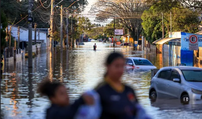 Imagem mostra, de forma borrada a não identificar as pessoas, uma mulher e uma filha; ao fundo, uma rua alagada em Eldorado do Sul, município do interior gaúcho