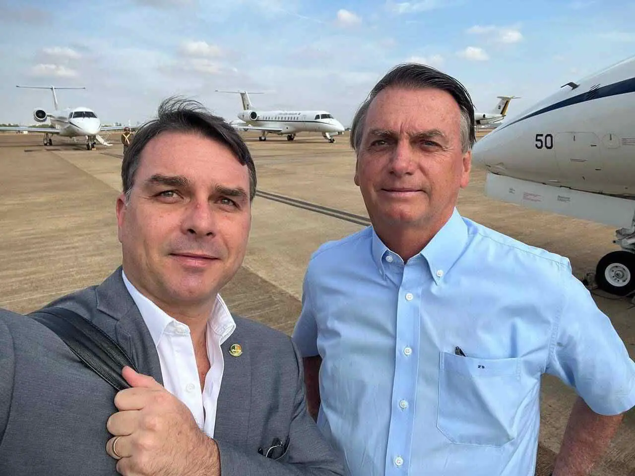 O Senador Flávio Bolsonaro (PL-SP) e ex-presidente do Brasil Jair Bolsonaro aparecem lado a lado em aeroporto, usando roupas sociais