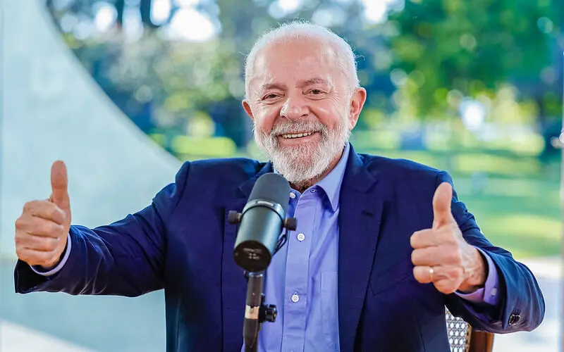 Lula admite possibilidade de disputar reeleição, em entrevista à Rádio CBN. Ele usa roupa social e está em frente a microfone