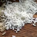 Imagem mostra grãos de arroz integral e arroz branco em cima de uma mesa de madeira; Conab confirma anulação de leilão para importação do grão