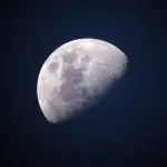Meia Lua em céu escuro, com superfície craterizada e áreas claras, contrastando com o fundo noturno