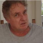 Saul Klein, filho do fundador da Casas Bahia, olha de frente para a câmera. Ele está de camiseta cinza. Atrás, uma sala com móveis comuns.