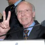 Mário Jorge Lobo Zagallo, vestido de terno preto e camisa azul, gesticulando com o sinal de 'paz e amor'