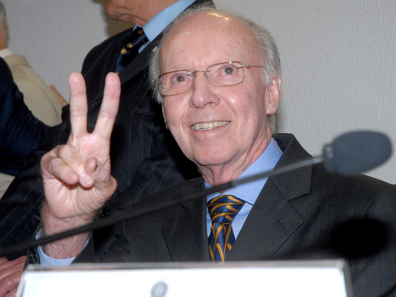 Mário Jorge Lobo Zagallo, vestido de terno preto e camisa azul, gesticulando com o sinal de 'paz e amor'