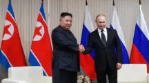 O ditador da Coreia do Norte, Kim-Jong-un, e o presidente da Rússia, Vladimir Putin. Na imagem, ambos aparecem apertando as mãos um do outro. Eles estão em uma sala, com a bandeira dos dois países ao fundo.