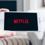Imagem de divulgação da Netflix exibe uma mão segurando um aparelho de celular; na tela, o logo do serviço de streaming