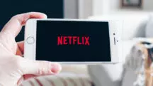 Imagem de divulgação da Netflix exibe uma mão segurando um aparelho de celular; na tela, o logo do serviço de streaming