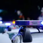 Imagem de carros da polícia, com a sirene ligada. Os veículos parecem alinhados, um atrás do outro