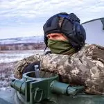 Um militar ucraniano, com o rosto coberto, em um tanque de guerra