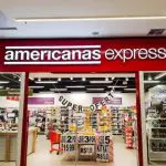 Imagem de uma loja da Americanas, com uma placa vermelho em cima e o nome da empresa na cor branca