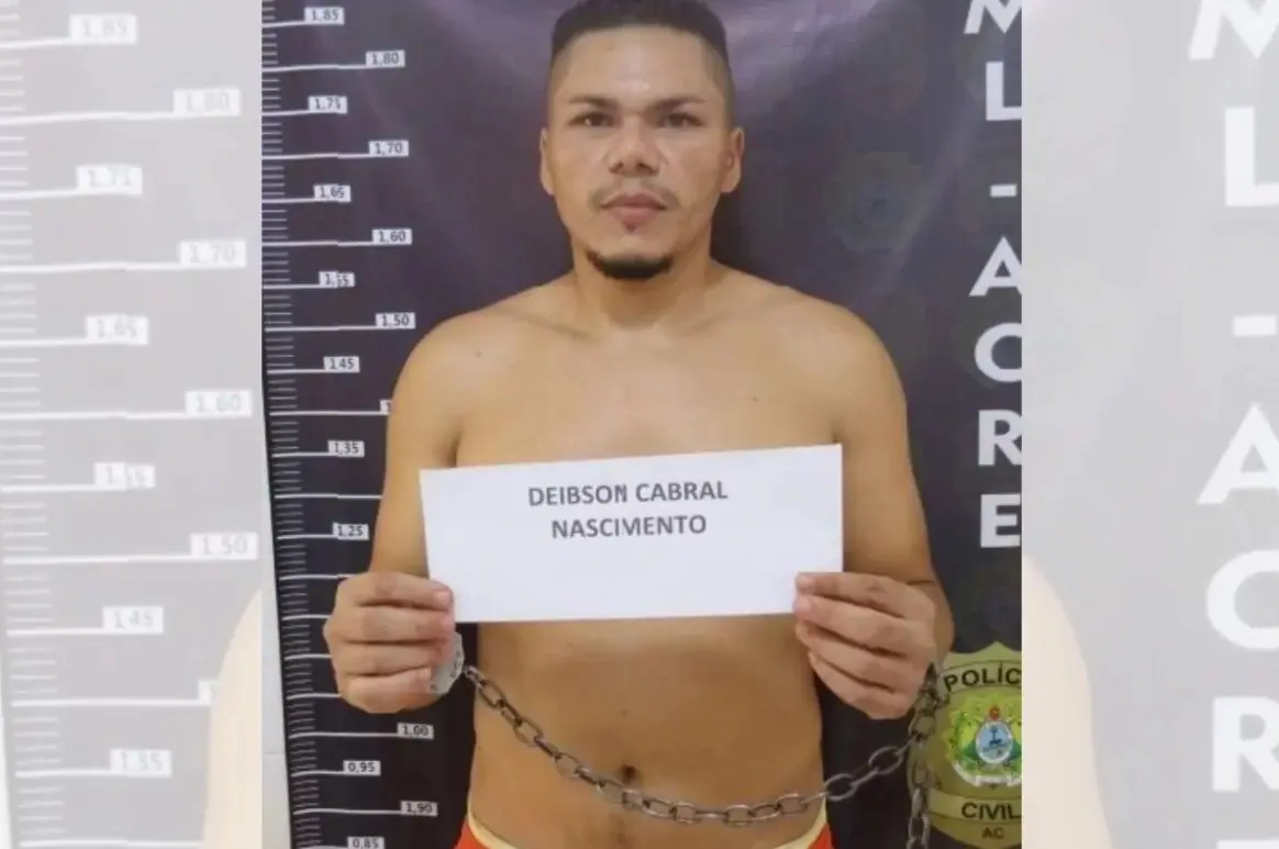 Deibson, integrante do Comando Vermelho, segura um papel com seu nome escrito. Ao fundo, um banner preto da Polícia Civil