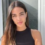 Ex-esposa de Daniel Alves, Joana Sanz, posa casualmente com um leve sorriso, junto a uma janela, exibindo sua beleza natural.