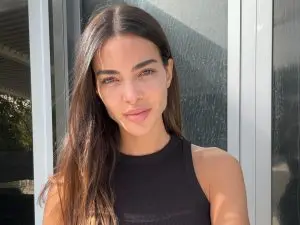 Ex-esposa de Daniel Alves, Joana Sanz, posa casualmente com um leve sorriso, junto a uma janela, exibindo sua beleza natural.