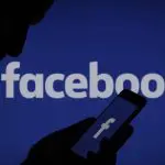 Foto ilustrativa mostra silhueta de pessoa com smartphone na mão, à frente de logo do Facebook, aplicativo da Meta