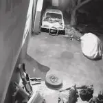 Imagem em preto e branco, da câmera de segurança da oficina alvo de furto no Tocantins. Na imagem, um carro ao fundo. Na frente, o "fantasma", com o corpo coberto por um pano branco.