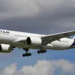 Avião da Latam de corredor duplo, pousando. Há um trem de pouso baixado, contra céu nublado