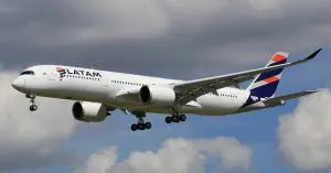 Avião da Latam de corredor duplo, pousando. Há um trem de pouso baixado, contra céu nublado