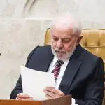 Lula com barba branca, lendo papel, trajando terno e gravata listrada, em cadeira dourada