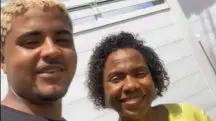 O jovem Marcos Vasconcelos ao lado da mulher que ele ajudou a salvar, em Nova Iguaçu. Ele tem cabelos loiros e usa camiseta preta. Ela tem cabelo enrolado e usa camisa amarela.