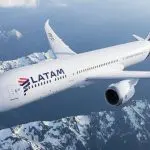 Um avião da Latam em pleno voo, com nuvens ao redor. A aeronave é branca