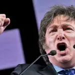 Javier Milei, presidente da Argentina, discursando. Ele veste um terno cinza com uma camisa azul