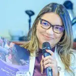 A primeira-dama, Janja, aparece sorrindo, com óculos e microfone nas mãos