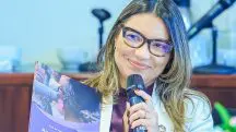 A primeira-dama, Janja, aparece sorrindo, com óculos e microfone nas mãos