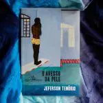 Um livro com tons de azul. Na capa, um homem negro, com cueca amarela, de costas para a parede e com as mãos no rosto.