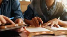 Imagem mostra duas pessoas à mesa, mas sem exibir os rostos, à mesa em momento de leitura