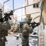 Soldados das Forças de Defesa de Israel em posição de combate frente a um prédio com terroristas do Hamas