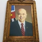 Um quadro do ex-governador de São Paulo José Serra. Ele aparece sorrindo, com terno preto e gravata vermelha escura.