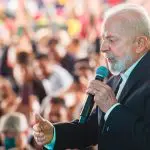 Presidente Lula usa terno preto e discursa com um microfone na mão