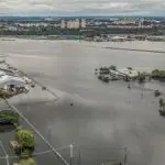 Pista do aeroporto Salgado Filho, em Porto Alegre (RS), tomada pela água; ao fundo, a Arena do Grêmio