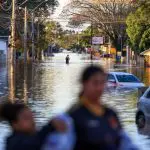 Imagem mostra, de forma borrada a não identificar as pessoas, uma mulher e uma filha; ao fundo, uma rua alagada em Eldorado do Sul, município do interior gaúcho