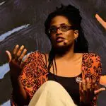 Imagem mostra autora Djamila Ribeiro sentada e gesticulando durante fala em evento