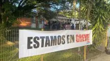 Foto mostra faixa na frente de escola com a mensagem "estamos em greve"