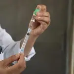 Vacina é administrada por profissional, com seringa na mão