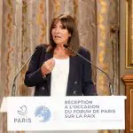 A prefeita de Paris, Anne Hidalgo, aparece em frente a púlpito, discursando em microfone. Ela, que usa roupa social, criticou Macron por convocar eleições antes das Olimpíadas
