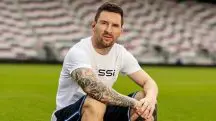 Lionel Messi veste camiseta branca e shorts preto, sentado no meio do campo de futebol