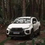 Carro da marca Fiat, uma Strada branca, aparece no meio de uma floresta