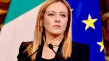 Giorgia Meloni critica acordo para cargos da União Europeia. Ela aparece em frente a púlpito, com bandeiras da Itália e da União Europeia ao fundo