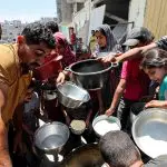 Palestinos se reúnem para receber comida, preparada em uma cozinha de caridade perto de casas destruídas na ofensiva militar israelense, em Khan Younis, no sul da Faixa de Gaza - 30/5/2024 | Foto: Ramadan Abed/Reuters