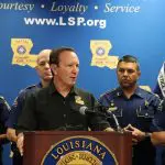 Governador da Louisiana, Jeff Landry, aparece em púlpito, vestindo camisa preta. Atrás dele, há menções ao Estado que ele governa