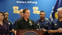 Governador da Louisiana, Jeff Landry, aparece em púlpito, vestindo camisa preta. Atrás dele, há menções ao Estado que ele governa