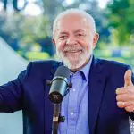 Lula admite possibilidade de disputar reeleição, em entrevista à Rádio CBN. Ele usa roupa social e está em frente a microfone