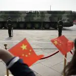 Espectadores acenam com bandeiras chinesas enquanto veículos militares carregando mísseis balísticos DF-41 desfilam durante uma parada para comemorar o 70º aniversário da fundação da China Comunista em Pequim - 1/10/19 | Foto: Mark Schiefelbein/AP
