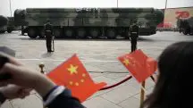 Espectadores acenam com bandeiras chinesas enquanto veículos militares carregando mísseis balísticos DF-41 desfilam durante uma parada para comemorar o 70º aniversário da fundação da China Comunista em Pequim - 1/10/19 | Foto: Mark Schiefelbein/AP